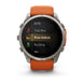 A Garmin smartwatch with a silver-toned metal case and an orange sport band, shown against a plain white background. The watch face displays a fitness menu with options like MTB, Trail Run, Row Indoor, Rucking, and Ski.