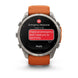 A Garmin smartwatch with a silver-toned metal case and an orange strap, shown on a clean white background. The watch screen displays an emergency message with a red SOS icon and a red text bubble reading, 'I have an emergency and I need you to send help.