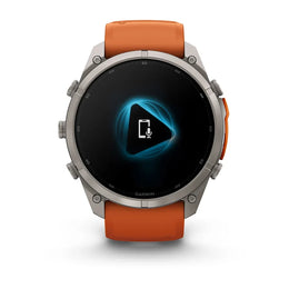 A Garmin smartwatch with a silver-toned metal case and an orange silicone strap, shown against a plain white background. The watch face is on and displays a blue and black digital interface.