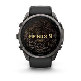 A Garmin Fenix 9 Pro smartwatch with a dark gray metallic case and a black strap, shown from the front on a white background. The watch face displays a black background with gold topographic lines and the text 'FENIX 9 PRO'.