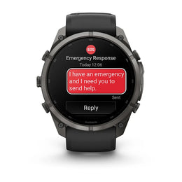 A Garmin smartwatch with a dark gray metallic case and black strap, shown on a white background. The watch screen displays an emergency message with a red SOS icon and a red text bubble reading 'I have an emergency and I need you to send help.
