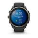 A Garmin smartwatch with a dark gray metallic case and a black strap, shown on a clean white background. The watch face is illuminated with a blue digital weather display.