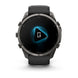 A Garmin smartwatch with a dark gray metallic case and a black strap, shown from the front on a white background. The screen displays a blue and white graphic.