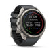 A Garmin smartwatch with a round silver-tone case and a dark gray silicone strap, shown at a three-quarter angle on a clean white background. The watch face displays fitness metrics.