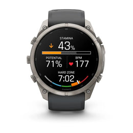 A Garmin smartwatch with a round silver-tone metal case and a dark gray silicone strap, shown on a clean white background. The watch face is active with various fitness and heart rate metrics displayed.