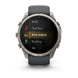 A Garmin smartwatch with a dark gray strap and a silver-toned metal case, displaying a fitness menu on its screen against a white background.