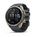 A rugged smartwatch with a round silver-tone metal case and a dark gray silicone strap, shown at a three-quarter angle on a white background. The watch face displays 'FENIX' and 'GARMIN' branding.