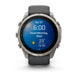 A Garmin smartwatch with a round silver-tone stainless steel case and a dark gray silicone strap, shown on a clean white background. The watch face is illuminated with a blue digital weather display.