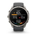 A Garmin smartwatch with a round silver-tone metal case and a dark gray silicone strap, shown on a clean white background. The watch face is active with various fitness and heart rate metrics displayed.