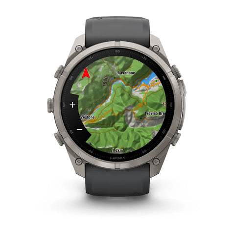 A Garmin smartwatch with a round silver-tone case and a dark gray strap, shown on a clean white background. The watch face is active with a green topographic map display.