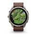 A Garmin smartwatch with a round silver-tone metal case and a brown leather strap, shown on a clean white background. The watch face displays a green topographic map.