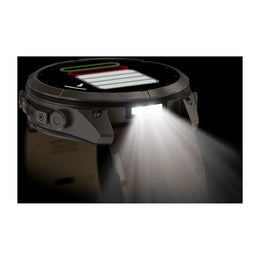 A rugged smartwatch with a circular display and angular side buttons, shown in profile with its front light turned on and casting a bright beam of light downward. The watch has a dark gray and black body with a light gray strap, set against a black backgr