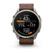 A Garmin smartwatch with a silver-toned metal case and a brown leather strap, shown on a clean white background. The watch face is active with various fitness and heart rate metrics displayed.
