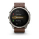 A Garmin smartwatch with a silver-toned metal case and a brown leather strap, shown on a clean white background. The watch face displays a fitness menu with options like MTB, Trail Run, Row Indoor, Rucking, and Ski.