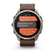 A Garmin smartwatch with a silver-toned metal case and a brown leather strap, shown on a clean white background. The watch screen displays a messaging app interface with orange and gray text bubbles.