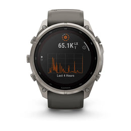 A Garmin smartwatch with a round silver titanium case and a dark gray silicone strap, shown on a clean white background. The watch face displays a black screen with an orange and white activity graph.