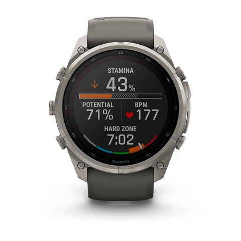 A Garmin smartwatch with a round silver-toned metal case and a dark gray silicone strap, shown against a plain white background. The watch face is illuminated with a black background displaying fitness metrics and a colorful progress bar.