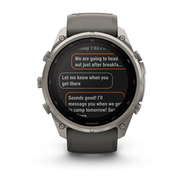 A Garmin smartwatch with a dark gray silicone strap and a silver-toned metallic case, shown against a plain white background. The watch face displays a messaging app screen.