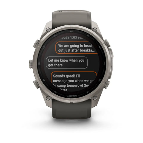 A Garmin smartwatch with a dark gray silicone strap and a silver-toned metallic case, shown against a plain white background. The watch face displays a messaging app screen.