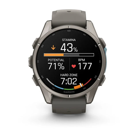 A Garmin smartwatch with a round dark gray titanium case and a matching dark gray silicone strap, shown against a plain white background. The watch face is active with various fitness and health metrics displayed.