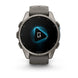 A Garmin smartwatch with a round metallic gray case and a dark gray strap, shown against a plain white background. The watch face displays a black screen with a glowing blue geometric icon and a white microphone symbol.