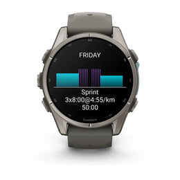 A Garmin smartwatch with a dark gray metallic case and a matching dark gray silicone strap, shown against a plain white background. The watch face is on and displaying a fitness screen with a running split and a bar chart.