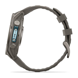 A rugged smartwatch shown from the side profile, featuring a dark gray textured silicone strap and a metallic gray case with a light blue accent on the side buttons.