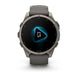 A Garmin smartwatch with a dark gray silicone strap and a metallic gray round case, shown against a plain white background. The watch face is black with a glowing blue geometric icon in the center.