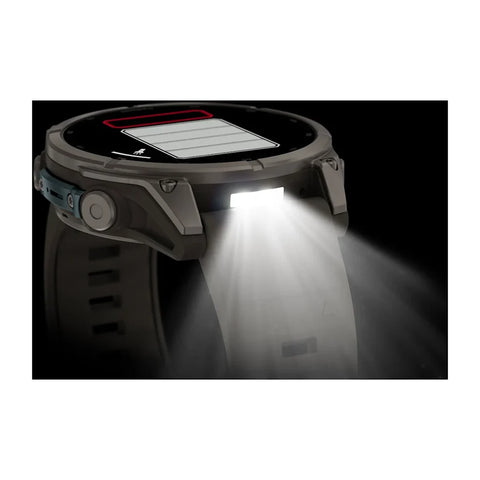 A rugged smartwatch with a circular display and side button, shown in a dark setting with its front light turned on, casting a bright beam of light forward. The watch face displays a battery icon.