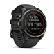A black Garmin smartwatch with a round dark gray case and a black textured strap, shown at a three-quarter angle on a white background. The watch face displays fitness metrics.