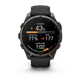 A Garmin smartwatch with a black strap and dark gray metallic case, shown on a clean white background. The watch face is active with various fitness metrics and colorful indicator rings.