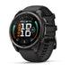 A Garmin smartwatch with a round black and dark gray case and a black textured strap, shown at a three-quarter angle on a white background. The watch face displays a digital fitness interface with the brand name 'GARMIN' visible at the bottom.