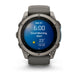 A Garmin smartwatch with a dark gray metallic case and matching dark gray strap, shown against a clean white background. The watch face displays a blue digital weather and time screen.