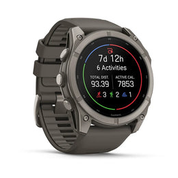A rugged Garmin smartwatch with a dark gray metallic case and a matching dark gray textured strap, shown at a three-quarter angle on a white background. The watch face is illuminated with a black digital display showing fitness metrics.