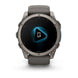 A rugged smartwatch with a dark gray metallic case and matching dark gray strap, shown from the front on a clean white background. The watch face displays a black screen with a glowing blue geometric icon and the Garmin logo at the bottom.