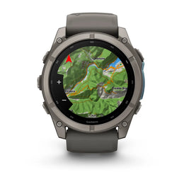 A Garmin smartwatch with a dark gray titanium case and matching silicone strap, shown on a clean white background. The watch face is illuminated with a green topographic map display.