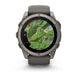 A Garmin smartwatch with a dark gray titanium case and matching silicone strap, shown on a clean white background. The watch face is illuminated with a green topographic map display.
