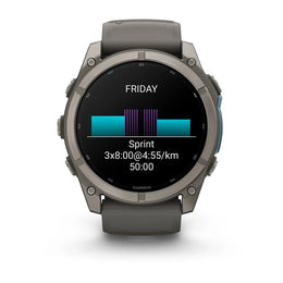 A Garmin smartwatch with a dark gray metallic case and a matching dark gray silicone strap, shown against a plain white background. The watch face is illuminated, displaying a fitness screen with a cycling-style bar graph and the text 'FRIDAY', 'Sprint', 