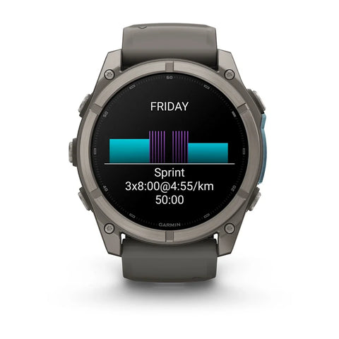 A Garmin smartwatch with a dark gray metallic case and a matching dark gray silicone strap, shown against a plain white background. The watch face is illuminated, displaying a fitness screen with a cycling-style bar graph and the text 'FRIDAY', 'Sprint', 