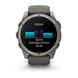 A Garmin smartwatch with a dark gray metallic case and a matching dark gray silicone strap, shown against a plain white background. The watch face is illuminated, displaying a fitness screen with a cycling-style bar graph and the text 'FRIDAY', 'Sprint', 