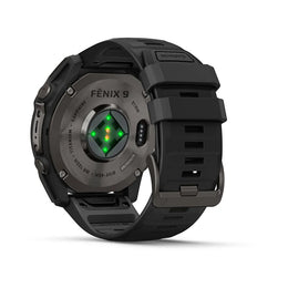 A rugged black smartwatch shown from the back, featuring a metallic dark gray case with 'FENIX 9' branding and a green heart icon on the backplate, alongside a black silicone strap. The NINJA band is visible on the upper right.