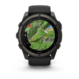 A rugged black Garmin smartwatch with a round face and black strap, shown on a clean white background. The screen displays a green topographic map with a red location marker.