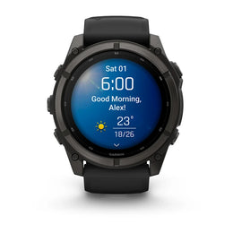 A Garmin smartwatch with a black rugged case and black strap, shown on a clean white background. The watch face is illuminated with a blue digital display showing the time, weather, and a greeting.