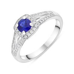 18ct white gold ring featuring a cushion-cut sapphire weighing 0.50 carats, surrounded by a cluster of diamonds totaling 0.25 carats. The ring is designed with a grain-set diamond split shank, adding elegance and sparkle to the overall look.