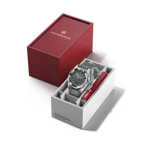 Silver watch with blue face in a white box, next to a red Victorinox box on a black background