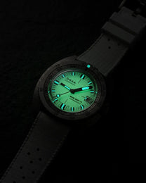 A DOXA 800 Auto-Balance watch with a dark gray textured strap and a glowing green dial, photographed in the dark to highlight its luminescent features.