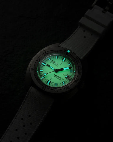 A DOXA 800 Auto-Balance watch with a dark gray textured strap and a glowing green dial, photographed in the dark to highlight its luminescent features.