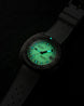 A DOXA 800 Auto-Balance watch with a dark gray textured strap and a glowing green dial, photographed in the dark to highlight its luminescent features.