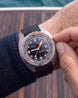 A close-up of a person's wrist wearing a DOXA diver watch with a black dial, black strap, and a silver-toned bezel featuring orange markings, with a hand adjusting the crown.