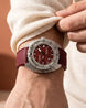 A close-up of a wrist wearing a dialux wrist watch with a textured burgundy leather strap and a matching burgundy dial, paired with a cream knit sweater.